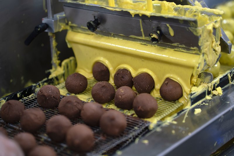 En anden maskine overtrækker dem med chokolade. Her er det gul chokolade, men bageriet har syv forskellige farver og smage, som de skifter imellem. I dag producerer bageriet lejlighedsromkugler, når danskerne for eksempel går til valg eller ser VM. 