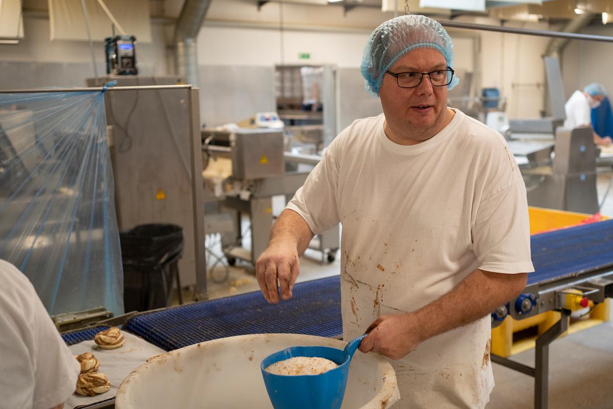 Efter en omgang æg, som sprøjtes på, er det tid til topping.  I dag er det Michael Nielsen, der står for at drysse overfladen med sukker og nødder. Snart har han en anden funktion. Det hold, der laver kanelsnurrer, roterer nemlig mellem stationerne. 